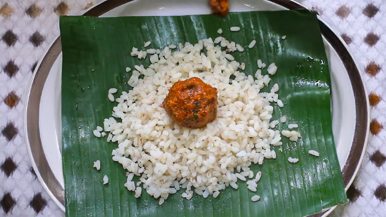 A bowl of spicy Kerala-style shallot chutney garnished with curry leaves, served with hot rice and curry on a traditional plate.