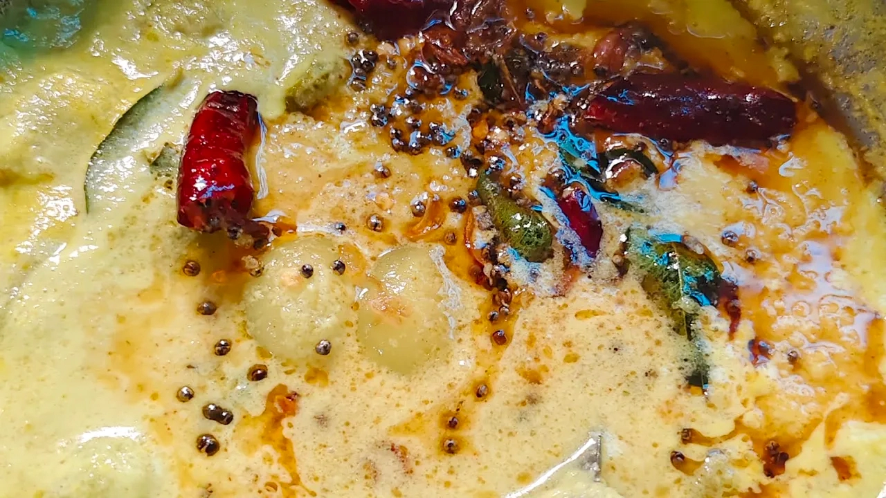 A vibrant bowl of Rambutan Curry garnished with curry leaves and mustard seeds, served alongside steamed rice on a traditional banana leaf.