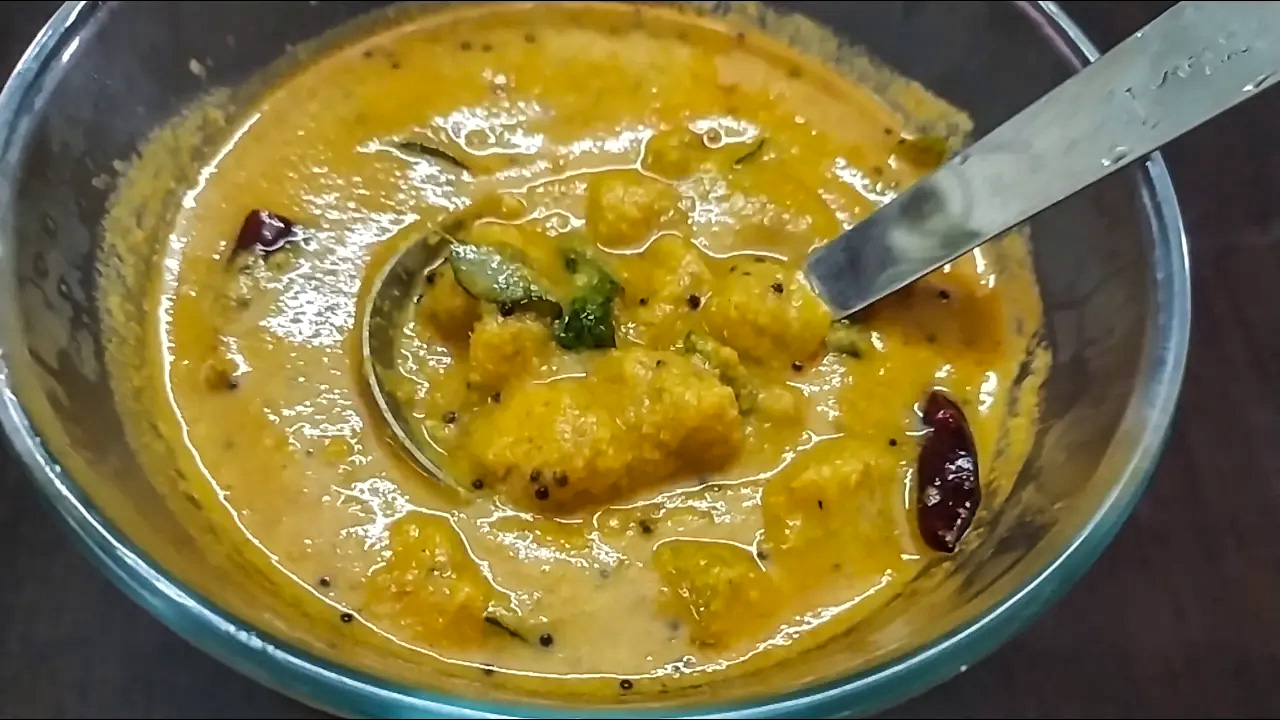 Close-up of a vibrant sweet potato curry in a bowl, garnished with curry leaves and tempered spices, showcasing its rich, creamy texture.