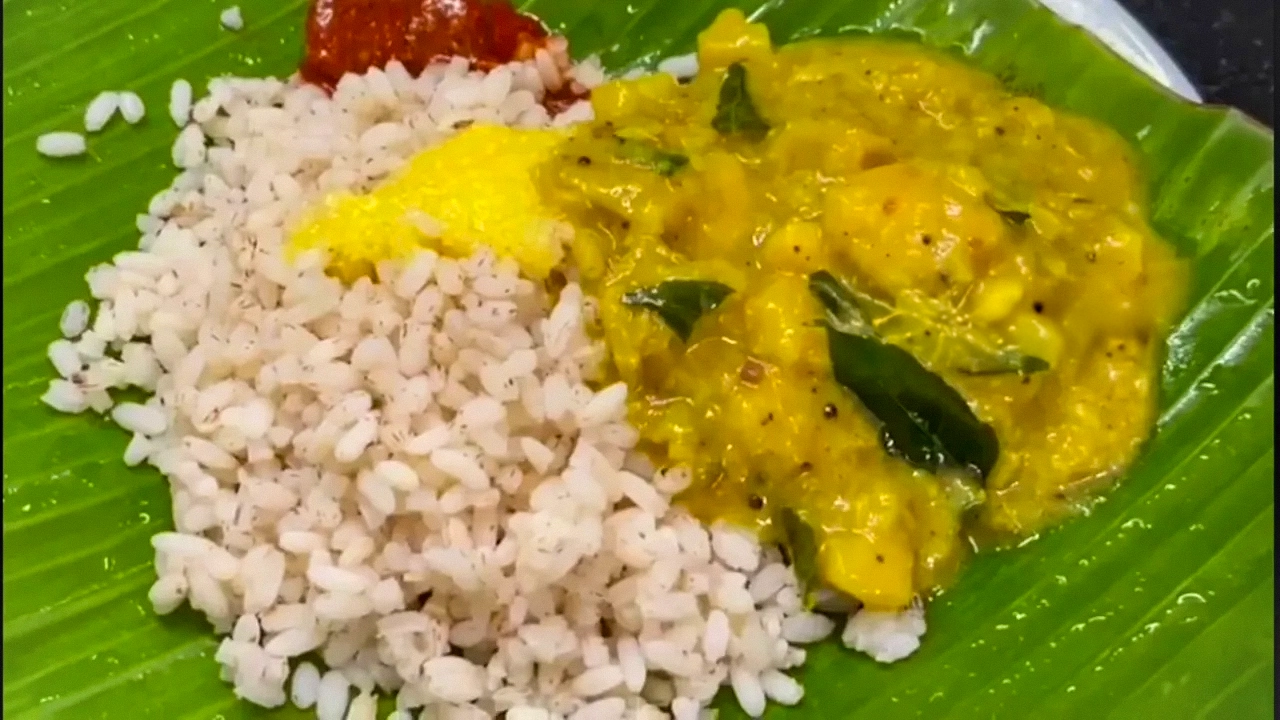 A bowl of traditional Kerala Mulakooshyam curry garnished with roasted coconut and curry leaves, served with a side of mango pickle.